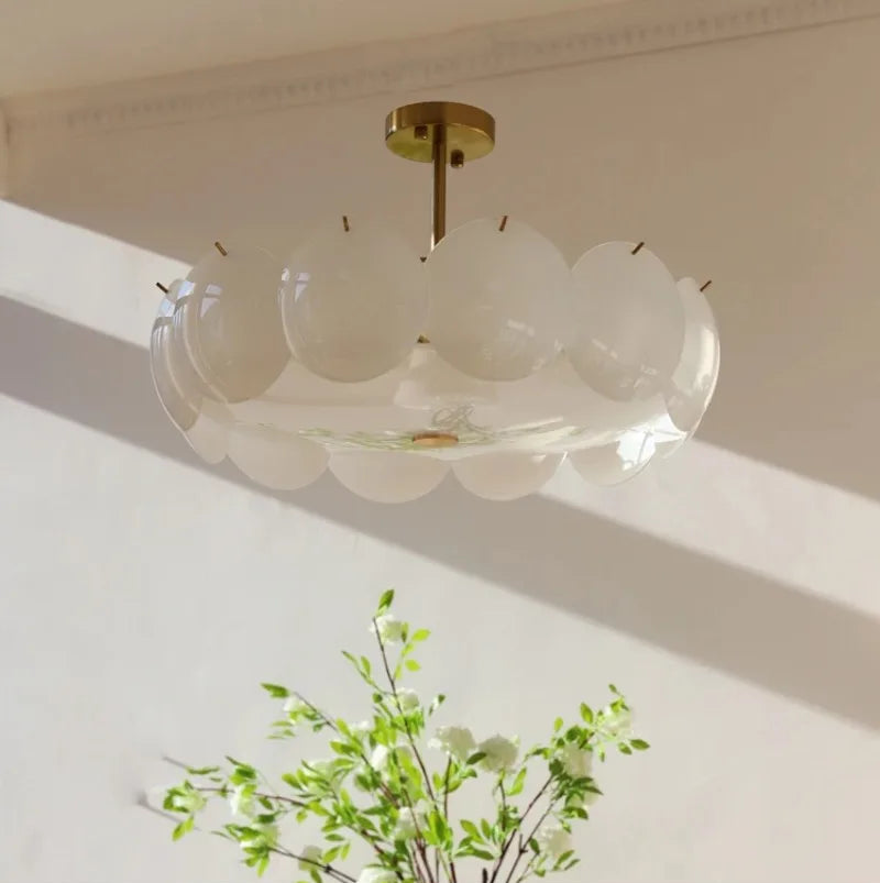 Ceiling light fixture with glass shades and gold fixture, with a plant in the foreground.