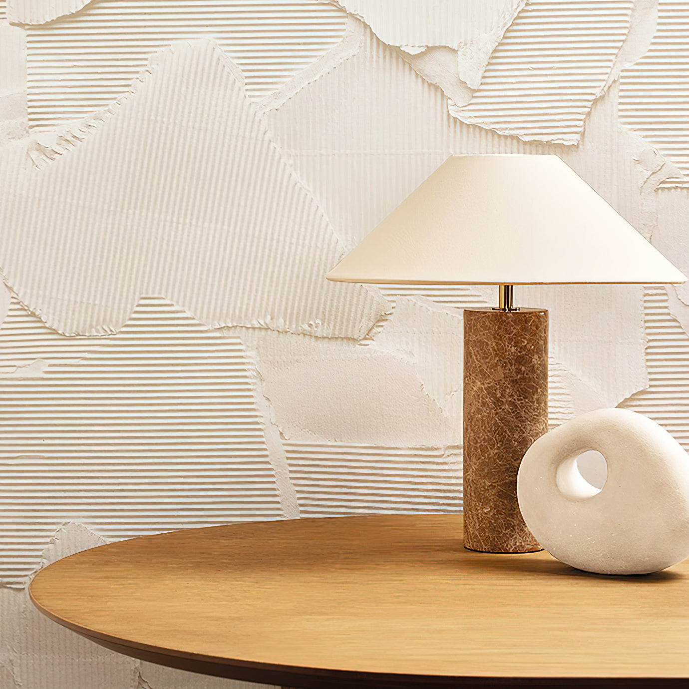 Table lamp with marble base and white shade on a wooden table against a textured wall.