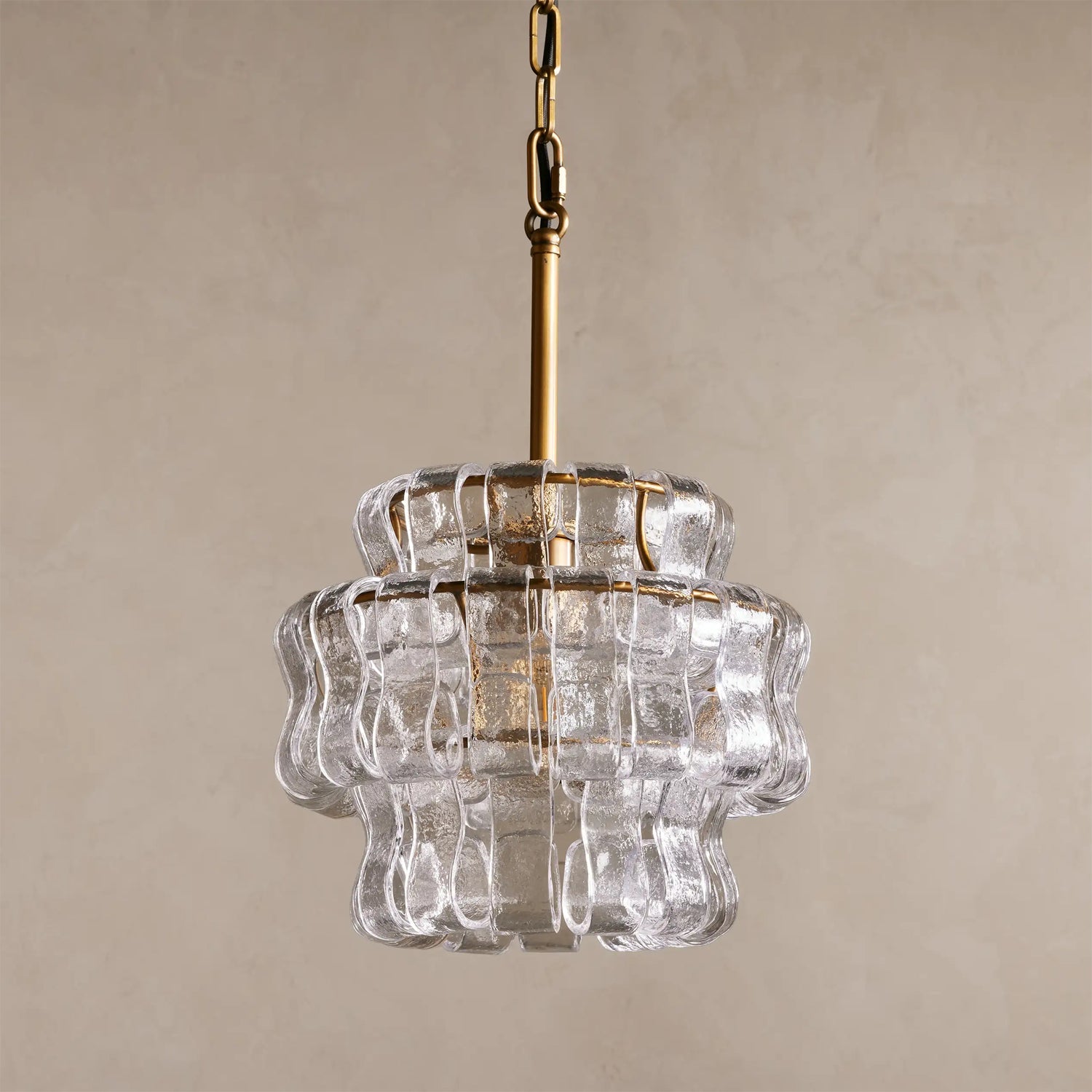 Clear glass pendant light with gold chain on a beige background