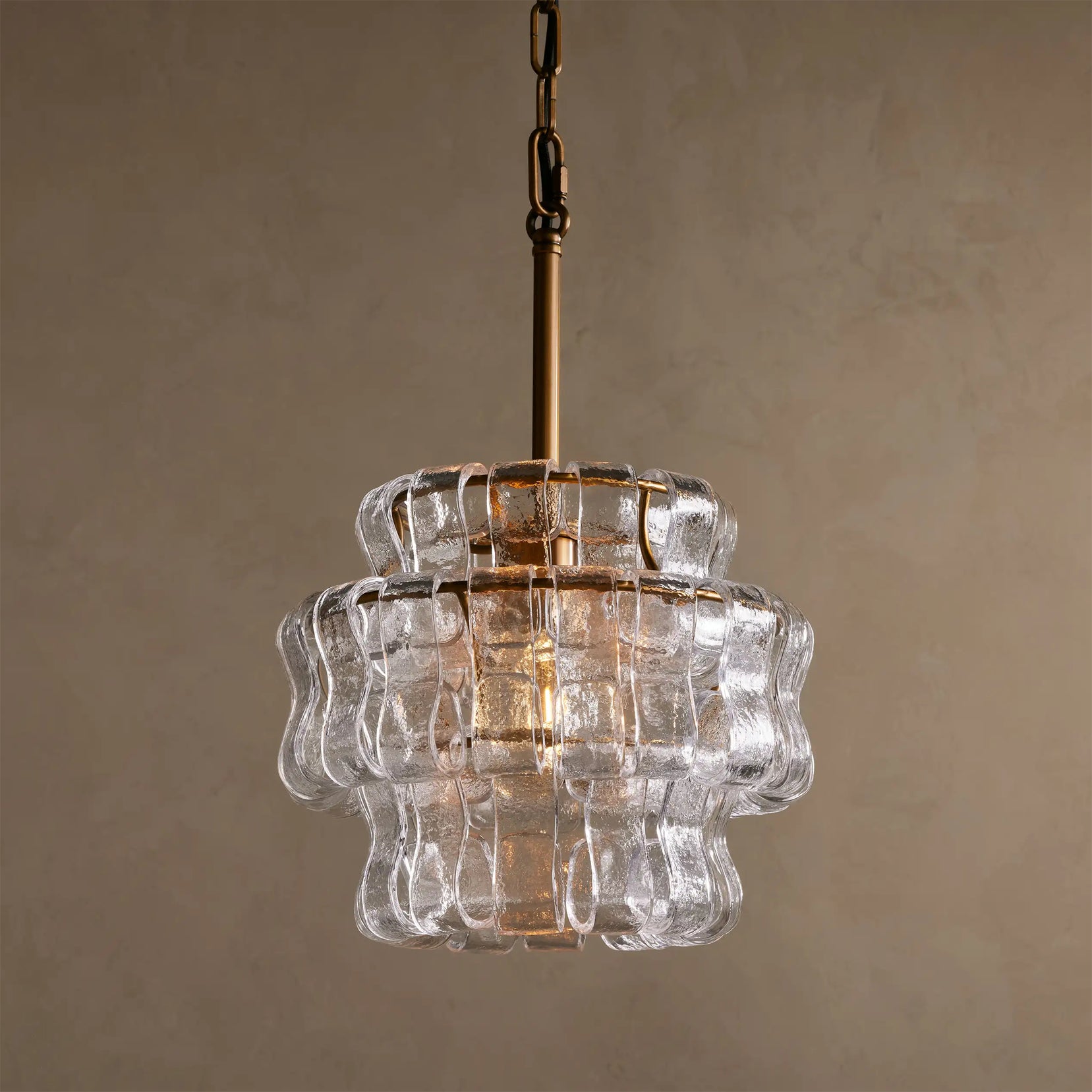 Clear glass pendant light with gold chain against a beige background