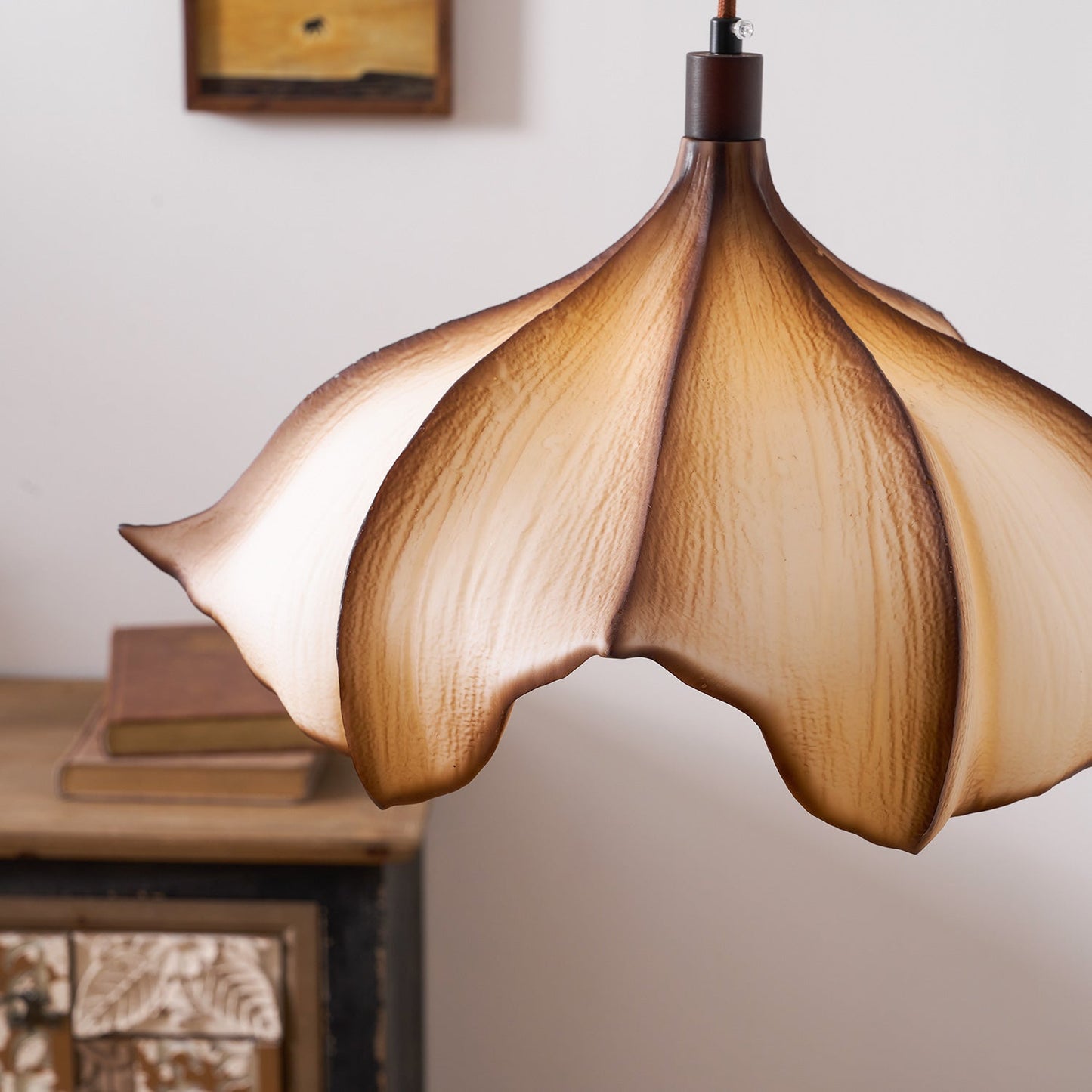 Floral-shaped pendant light with a warm glow in a softly blurred room setting.