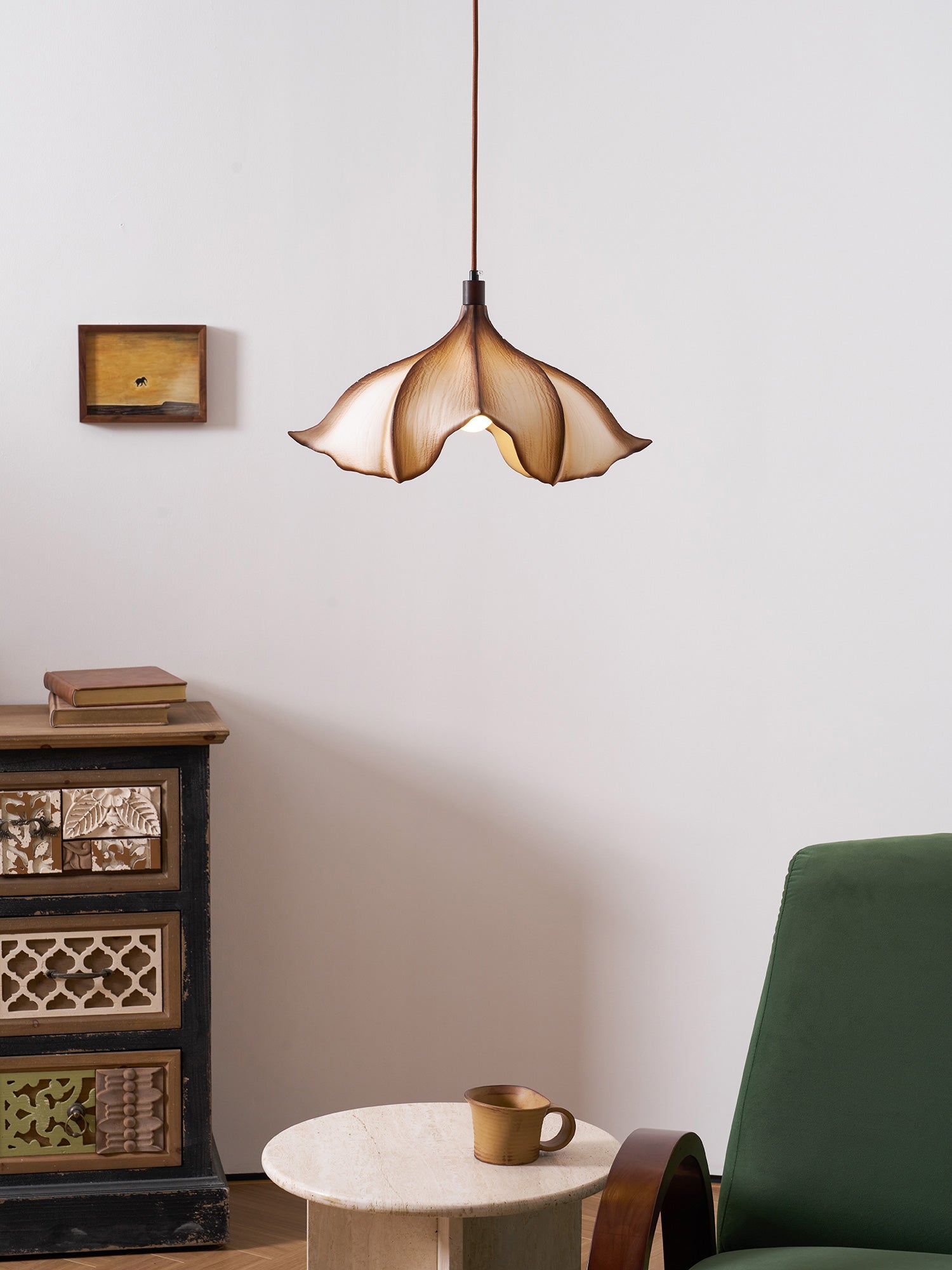 Modern pendant light hanging in a room with a green chair and wooden cabinet.