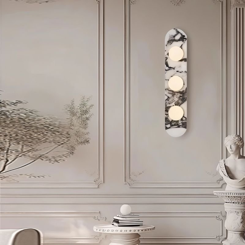 Decorative wall sconce with circular lights on a wall with framed artwork and a statue.